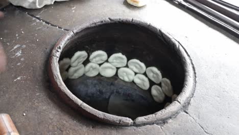 Food-vendor-putting-flat-dough-in-clay-oven-to-make-grilled-Chinese-flat-bread-or-"Huping"-in-traditional-way