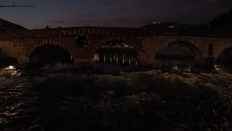Aerial-Drone-Shot-passing-throught-Ponte-Pietra-Bridge-in-Verona-at-Night-till-S