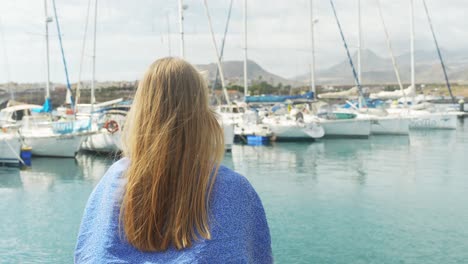 Hermosa-Mujer-Rubia-Admira-El-Muelle-Y-El-Paisaje-Montañoso-De-Tenerife,-Vista-Posterior