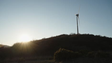 Einsame-Windkraftanlage-Auf-Einem-Hügel,-Der-Sich-Bei-Tagesanbruch-Vor-Der-Hellen-Sonne-Abhebt