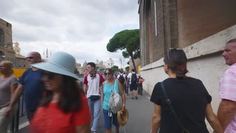 Rome-Immersive-POV:-Moving-In-Busy-Streets-to-Chiesa-Santi-Luca-e-Martina,-Italy,-Europe,-Walking,-Shaky,-4K-|-Elderly-Couple-Holding-Hands-While-Walking-Through-Crowd