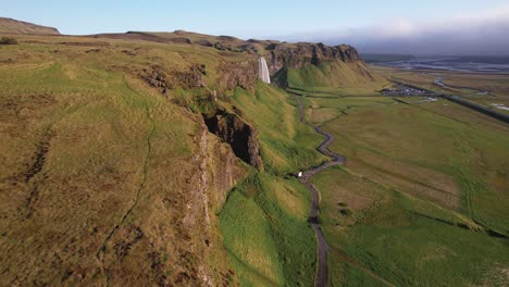 Aerial-view-of-majestic-waterfalls-in-lush-green-Icelandic-landscape-with-meandering-river-and-clear-skies