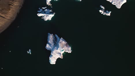 Luftaufnahme-Von-Gletschereis,-Das-Im-Dunklen-Wasser-Schwimmt-Und-Schatten-Auf-Die-Eisige-Oberfläche-Wirft