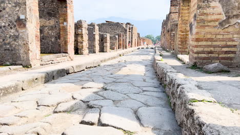 Ancient-ruins-of-a-Roman-street,-with-columns-and-stone-pavement,-under-a-sunny-sky---Pompeii