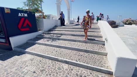 Travelers-Near-Cafe-and-Steps-|-Oia-Santorini-Greece-Greek-Island-in-Aegean-Sea,-Travel-Tourist-Vacation-Immersive-Moving-Walk-Along-Crowds-Shopping-in-White-Marble-Cliffside-and-City,-Europe,-4K