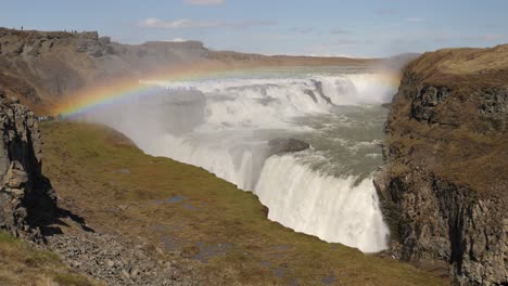 Majestic-waterfall-with-vibrant-rainbow-across-the-rocky-terrain-under-a-clear-sky-in-Iceland