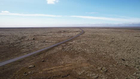 Vista-Aérea-De-Una-Carretera-Desierta-Que-Atraviesa-Un-Paisaje-árido-Bajo-Un-Cielo-Despejado-En-Islandia