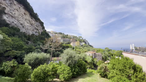 A-lush-hillside-town-overlooking-the-sea,-with-terraced-buildings-and-abundant-greenery-under-a-bright-sky---Sorrento