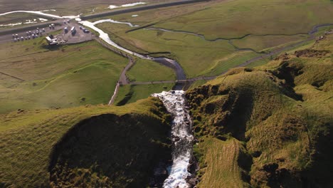 Aerial-view-of-a-cascading-waterfall-amid-green-hills-with-a-walking-path-and-tributary-rivers-in-Iceland