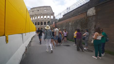 Rome-Immersive-POV:-Moving-In-Busy-Streets-to-Chiesa-Santi-Luca-e-Martina,-Italy,-Europe,-Walking,-Shaky,-4K-|-Long-Line-Of-Tourists-Near-Sign-By-Colosseum