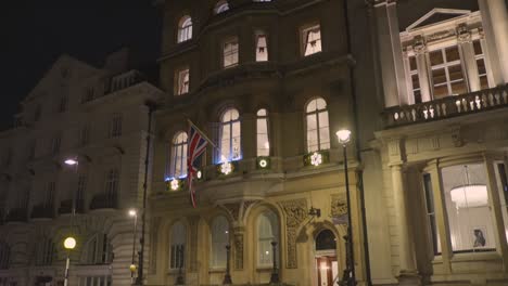 Filmische-Aufnahme-Der-Architektur-Eines-Vintage-Gebäudes-Mit-Der-Flagge-Des-Vereinigten-Königreichs-Neben-Einer-Belebten-Straße-Während-Der-Nacht-In-London,-England