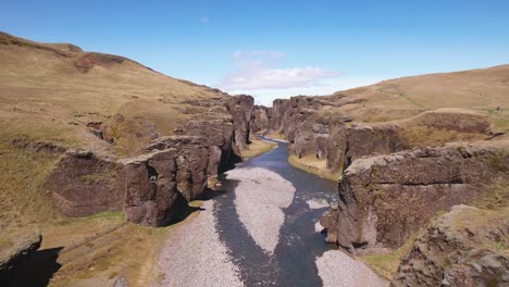 Río-Sinuoso-A-Través-De-Un-Espectacular-Paisaje-De-Cañón-Bajo-Un-Cielo-Despejado,-Destacando-La-Hierba-Verde-Y-La-Naturaleza-Serena,-Tomado-Desde-Una-Perspectiva-Aérea-En-Islandia