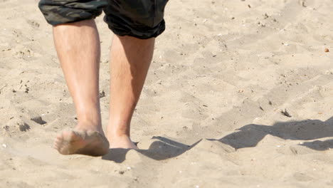Close-up-of-a-person-walking-barefoot-on-a-sandy-beach,-with-a-focus-on-the-feet-and-sand