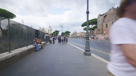 Rome-Immersive-POV:-Moving-In-Busy-Streets-to-Chiesa-Santi-Luca-e-Martina,-Italy,-Europe,-Walking,-Shaky,-4K-|-Teenagers-Sitting-On-Phone-As-Tourists-Pass-By