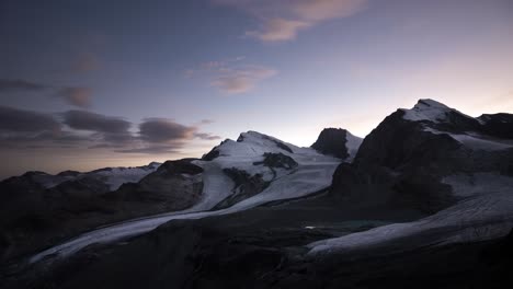 Timelapse-of-the-Allalin-and-Hohlaub-glaciers-from-the-viewpoint-near-Britattanihütte-in-Saas-Fee,-Valais,-Switzerland-with-a-colorful-sky-at-sunset-with-Rimpfischhorn-and-Strahlhorn-in-view