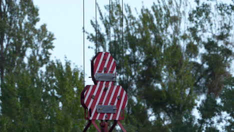 Red-and-white-construction-clamps-suspended-by-cables-against-a-backdrop-of-trees,-indicating-construction-or-repair-work