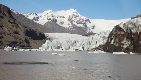 Gletscherlagune-Mit-Schwimmendem-Eis-Und-Schneebedeckten-Bergen-Unter-Einem-Klaren-Blauen-Himmel-In-Island