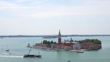 Aerial-of-merchant-ship-sailing-by-San-Giorgio-Maggiore-in-Venice,-4K