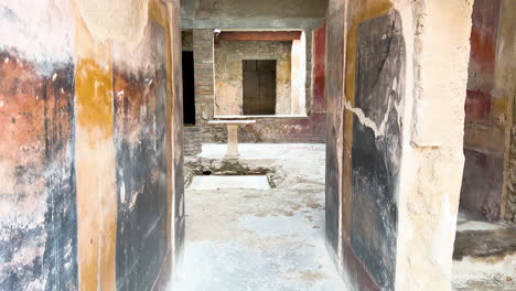 The-interior-of-an-ancient-Roman-house-in-Pompeii,-showing-faded-frescoes-on-the-walls-and-a-central-stone-table-in-an-atrium