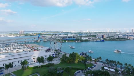 Aerial-view-showing-cruising-boats-at-Miami-Bayside-with-harbor-and-ferris-wheel-during-sunny-day-with-blue-sky