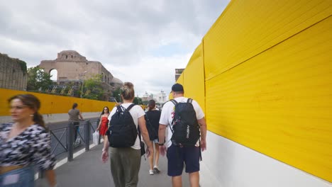 Rome-Immersive-POV:-Moving-In-Busy-Streets-to-Chiesa-Santi-Luca-e-Martina,-Italy,-Europe,-Walking,-Shaky,-4K-|-Couple-Walking-On-Busy-Sidewalk-Near-Yellow-Construction-Walls