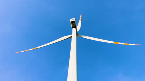A-towering-wind-turbine-with-three-long-blades-against-a-clear-blue-sky,-representing-renewable-energy-and-modern-technology