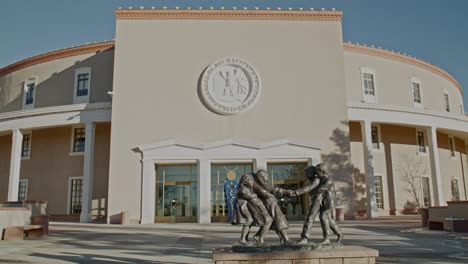 Edificio-Del-Capitolio-Del-Estado-De-Nuevo-México-En-Santa-Fe,-Nuevo-México-Y-Niños-Jugando-Estatua-Con-Muñeca-Moviéndose-De-Izquierda-A-Derecha