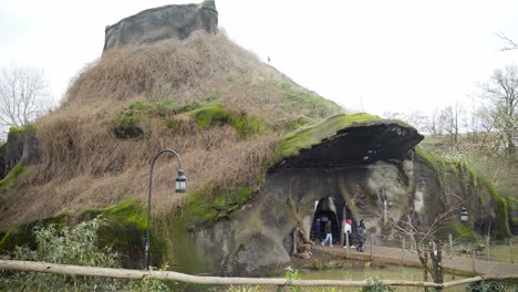 Gorilla-cave-in-Pairi-Daiza-zoo-park,-tourists-walking-outside-volcano-architectural-building