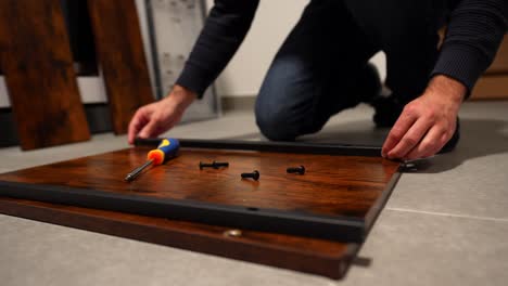 Close-up-of-male-hands-assembling-wooden-furniture-with-screwdriver-on-floor