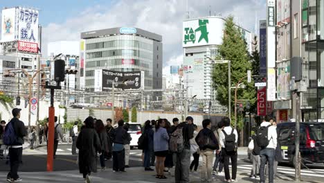 Pedestrians-traverse-alongside-the-east-exit-at-Shinjuku-Station-in-Tokyo,-Japan,-navigating-the-bustling-urban-scene-with-seamless-motion