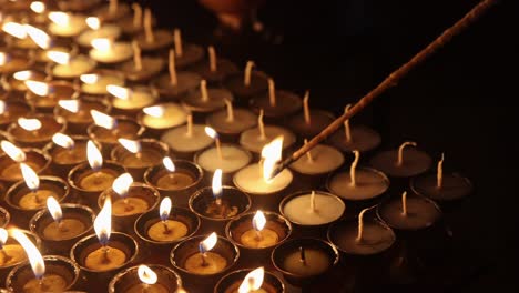Detailed-closeup-of-lighting-symbolic-prayer-tea-light-candles-with-traditional-wick-wooden-lighter-at-night