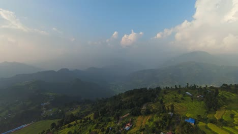 Cinematic-drone-flight-over-idyllic-mountains-with-asian-villages-and-fog-covering-mountain-range-in-background-at-sunset---Nepal,-Asia