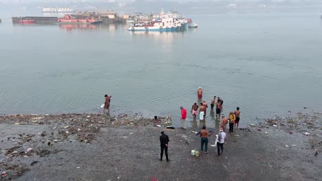 Top-shot-of-few-men-bathing-at-shore-of-a-sea-with-a-boat-at-the-background-during-winter-morning-in-Kolkata-,-India