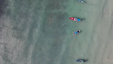 Aerial-Birds-Eye-View-Along-Row-Of-Moored-Empty-Boats-Off-Sairee-Beach-In-Shallow-Waters