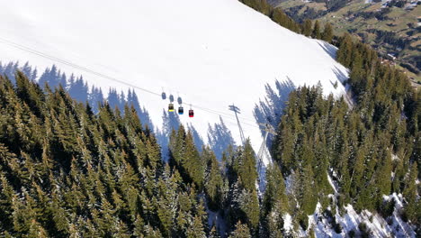 Aerial-shot-of-Tschentenegg-cable-car-moving-downhill-followed-by-shadows-on-the-snow