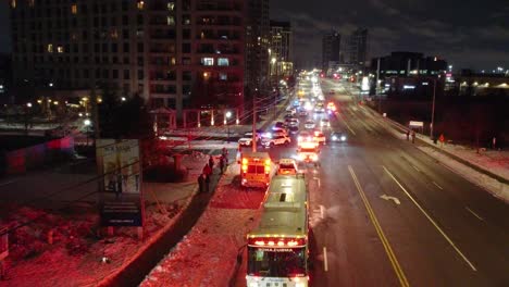 Nighttime-city-scene-with-emergency-vehicles,-snowy-roads,-and-buildings