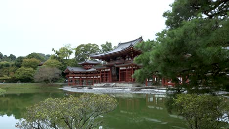 Cinematic-profile-view-of-famous-Byodo-in-Buddhist-temple-surrounded-by-water-and-trees-with-a-beautiful-landscape-during-a-cloudy-day-in-Uji,-Kyoto,-Japan