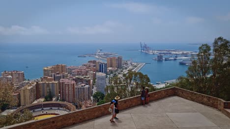 Tourists-look-at-the-view-of-city-buildings-on-the-edge-of-the-pier-from-a-building-on-the-hills-in-the-city-of-Malaga,-Spain