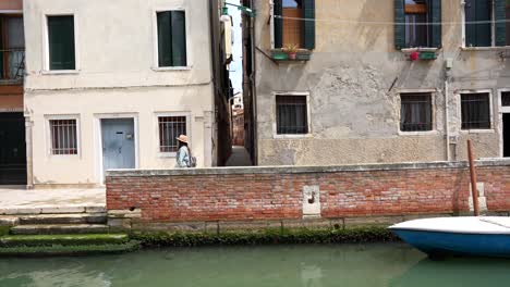 Tourist-strolls-Venetian-streets-with-charming-ancient-houses,-canal-side