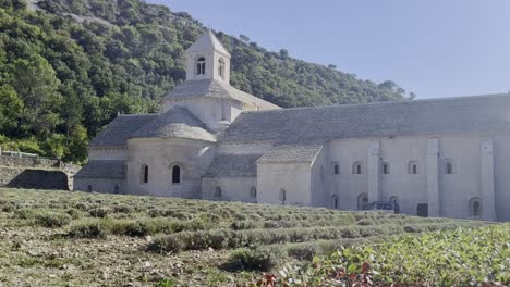 Large-monastery-in-France-with-bell-tower-and-stone-buildings-with-small-hills-in-the-background
