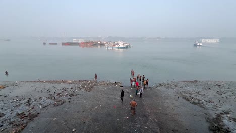 Wide-angle-top-shot-of-men-bathing-at-a-riverbank-of-Hooghly-river-during-morning-in-Kolkata,-India