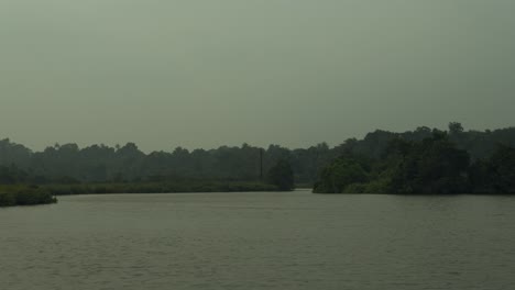 Tranquil-lake-with-surrounding-greenery-under-a-hazy-sky,-hinting-at-early-morning-serenity-or-dusk-calmness