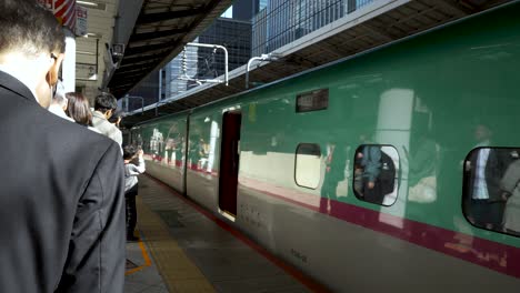 Travelers-form-a-queue-to-green-E5-and-H5-Series-Shinkansen-trains-at-Tokyo-station-in-Japan,-patiently-awaiting-their-turn-to-embark-on-a-high-speed-rail-journey