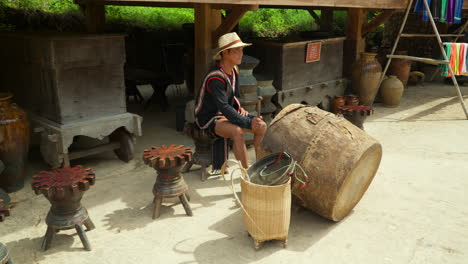Cu-Lan-Village-in-Da-Lat-City---Vietnamese-Man-Performer-Plays-on-Ethnic-Big-Drum-at-Street,-Old-Retro-Furniture-in-Backdrop---slow-motion