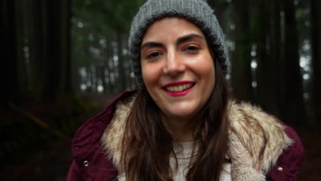 Close-up-of-smiling-woman-in-dark-forest-wearing-beanie-for-cold