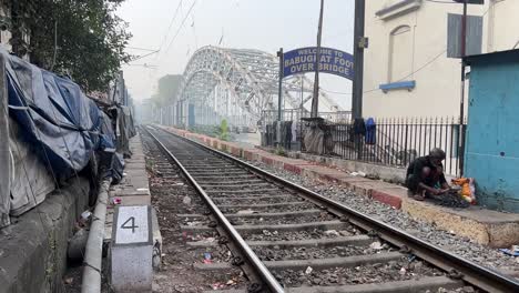 Cinematic-shot-of-an-empty-rail-line-beside-a-foot-overbridge-and-man-breaking-charcoals-during-morning-in-Kolkata,-India