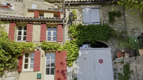 Small-French-house-with-beautiful-windows-at-the-foot-of-a-hill-with-another-house,-some-plants-and-a-large-rock-in-the-background-in-good-weather