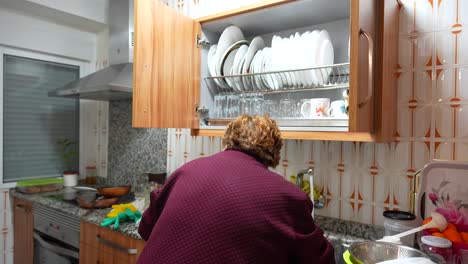 Elderly-woman-in-purple-clothing-cleaning-and-organizing-dishes-in-a-home-kitchen