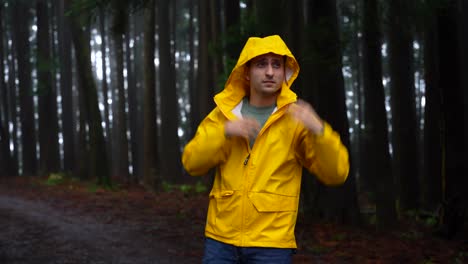 Man-braves-eerie-forest-rain,-zips-yellow-raincoat-in-discomfort