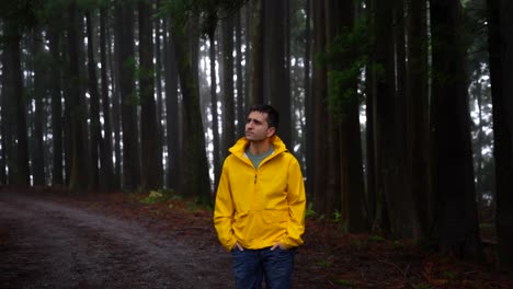 Medium-shot-of-man-in-yellow-raincoat-waiting-in-dark,-scary-forest